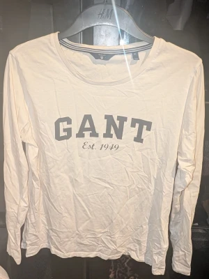 Vit långärmad tröja från GANT - Säljer en vit långärmad topp från GANT med trycket 'GANT Est. 1949' på bröstet. Klassisk rund halsringning och mjukt material som känns skönt mot huden. Inga synliga fläckar eller defekter. Skapa en bundle för bättre pris