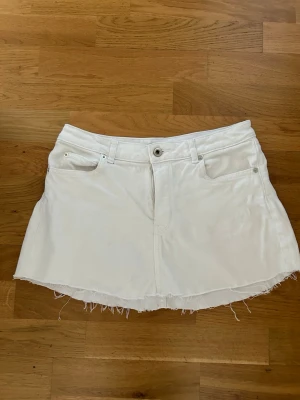 Vit jeanskjol med fransig kant - Vit kort jeanskjol rå, fransig kant nertill. Kjolen har bälteshällor och knappstängning framtill. Hitta ingen storlek men skulle säga att den sitter som en S. Den har inga fläckar eller andra defekter😊💕