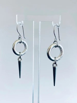 Silvriga örhängen i stål med ring och spike - Coola örhängen i silverfärg med rund ring och spetsig spike-hängande detalj. Ringen har ett mönstrat parti som ger extra edge. Perfekt för dig som gillar att sticka ut och vill ha något unikt till din stil.
