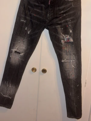 Svarta distressed jeans Dsquared2 - Säljer ett par svarta jeans från Dsquared2 med slitningar, tryck och färgstänk för en edgy look. Jeansen har dragkedjegylf och smal passform. Materialet är klassisk denim med coola detaljer och patchar på benen. Perfekta för dig som gillar streetwear.