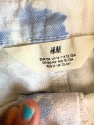 Blåvit tie-dye shorts från H&M - Säljer ett par blåvita tie-dye shorts från H&M med klassisk femficksmodell och knappgylf. Shortsen har bälteshällor och är tillverkade i ett mjukt bomullstyg. Perfekta för dig som vill ha en chill och trendig sommarstil.