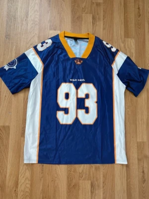 Lila jersey - Säljer en blå och vit sporttröja med gula detaljer och stort nummer 93 både fram och bak. På bröstet och ryggen står det 'Wild Soul'. Tröjan har korta ärmar och V-ringad krage i gult. Perfekt för dig som gillar sportig stil.