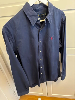 Mörkblå skjorta från Ralph Lauren - En näst intill ny skjorta ifrån Ralph Lauren, i storlek L men är slim fit så funkar på M mer. Priset är förhandlingsbart så bara att buda på.