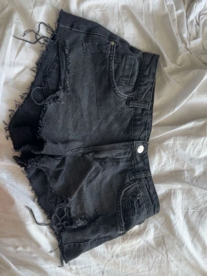 Svarta jeansshorts med fransig kant - Säljer ett par svarta jeansshorts från Zara med fransiga kanter och slitna detaljer, men är använda fåtal gånger. Low/midrise Uttvättad svart färg. Storlek 36