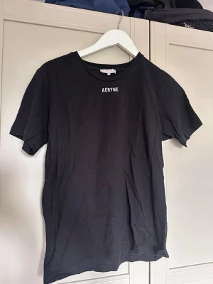 Svart t-shirt från Aéryne - Säljer en svart t-shirt från Aéryne med enkel design och rund hals. T-shirten har korta ärmar och en liten vit logga på bröstet. Perfekt basplagg till garderoben och gjord i mjuk bomull för skön känsla.