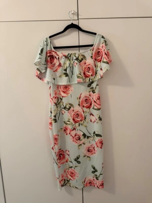 Ljusblommig offshoulder klänning - Superfin ljus klänning med stora rosa blommor och offshoulder-modell. Klänningen har volang upptill och är i en mjuk, följsam passform. Perfekt för sommarens alla tillfällen!