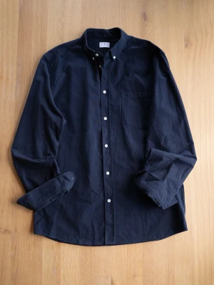 Asket Black / Dark Navy Oxford Button Down Shirt, size XL - Klassisk mörkblå / Svart skjorta från ASKET i bomull med button-down krage och vita knappar. Skjortan har lång ärm och en bröstficka, perfekt för en clean och stilren look.