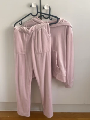 Ljusrosa velour loungewear-set - Supermysigt loungewear-set i ljusrosa velour med hoodie och dragkedja framtill. Tröjan har stora fickor och ribbade muddar, byxorna har resår i midjan och praktiska fickor. Perfekt för chill dagar hemma och riktigt skönt material.