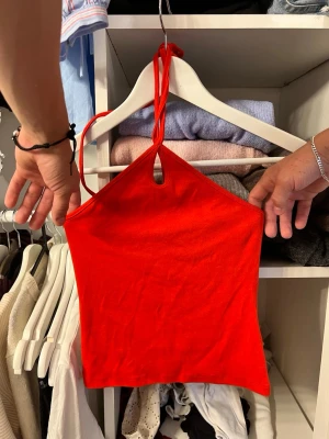 Röd ärmlös halterneck topp - Snygg röd halterneck topp med knyt i nacken och liten öppning framtill.  Helt ny med lapp kvar!
