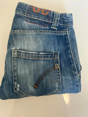 Dondup jeans  - Org slitningar från fabrik W30 l30 Säljer ett par blå jeans med snygg tvätt och slitningar. Jeansen har unika detaljer på bakfickorna, inklusive en dekorativ söm och liten metallspänne. Klassisk femficksmodell och normal passform. Perfekta för dig som gillar en avslappnad men trendig stil.