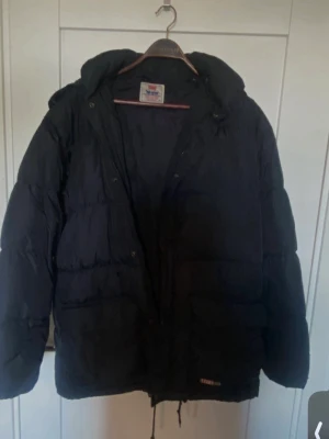 Svart Levis jacka med luva stor M - Svart Levi's dunjacka med huva. Jackan har dragkedja och knappar framtill samt fickor med lock. Det finns även en liten Levi's-logga nedtill på framsidan.  välvårdad använt kanske 2-3 gånger är en stor M