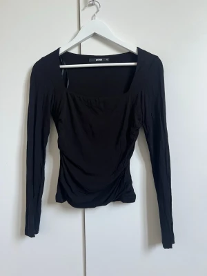 Svart och vit långärmad topp - Två långärmade toppar i svart och vitt med fyrkantig ringning och figurnära passform. Tillverkade i mjukt material som ger en snygg drapering över magen. Perfekta basplaggen att ha i sin garderob. Topparna är precis samma modell och storlek, XS