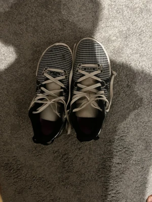 Lebron basketboll skor - Säljer ett par Nike Witness VII sneakers i svart och vitt med rutmönstrad mesh-överdel och vita snören. Skon har en chunky sula med transparent detalj på hälen och textdetalj på sidan. Perfekta för dig som gillar sportig och modern stil. Den är lite sliten på baksidan av skorna har inte kvar skokartongen. Ord pris 934 kr.
