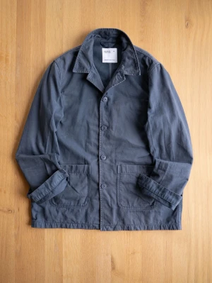 Washed Blue Chore Jacket från ISTO - Stilren mörkblå overshirt från ISTO i bomull. Klassisk krage, knäppning framtill med fyra knappar och två stora fickor framtill. Perfekt lager på lager-plagg med avslappnad passform och snygga detaljer vid sömmarna.