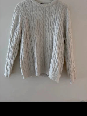 Vit kabelstickad tröja - Kabelstickad tröja i mjuk vit färg med rund halsringning och långa ärmar. Klassisk flätstickning över hela tröjan och ribbade muddar vid ärmslut och nederkant. Perfekt för lager på lager under kyliga dagar.