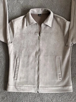 LJUSGRÅ SKINNJACKA  -  SKINNJACKA MED DRAGKEDJA ✅ DEN ÄR MOCKAD SKÖNT OCH MJUKT MATERIAL ✅I STORLEK XS ✅ PASSAR PERFEKT INFÖR HÖSTEN 🍂 INGA DEFEKTER PÅ PLAGGET ✅