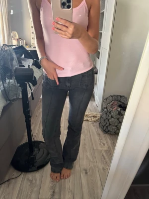 Mörkgrå raka jeans med sömdetaljer - Säljer ett par mörkgrå jeans med raka ben och markerade sömmar framtill. Jeansen har bakfickor med knappdetalj och sitter snyggt på kroppen. Perfekta till en enkel topp eller hoodie. Materialet känns mjukt och stretchigt för extra komfort.