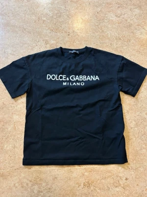 Svart Dolce & Gabbana t-shirt - Snygg svart t-shirt från Dolce & Gabbana med vit logga och Milano-tryck på bröstet. Klassisk rund halsringning och korta ärmar. Tillverkad i mjuk bomull för en bekväm känsla och stilren look. Ny aldrig använd, storlek xs men är oversize