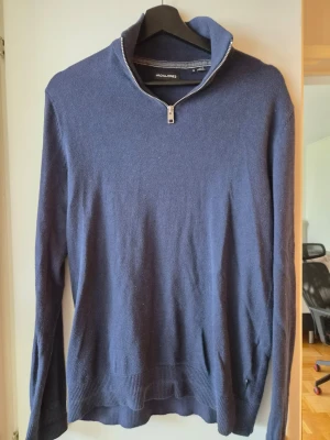 Marinblå stickad tröja Jack & Jones - Snygg marinblå stickad tröja från Jack & Jones med halv dragkedja i halsen. Tröjan har långa ärmar, ribbade muddar och en mjuk, tunn stickning som passar perfekt till lager på lager. Enkel och stilren design.