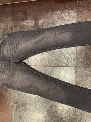 Mörkgrå slim fit jeans - Snygga mörkgrå slim fit jeans med klassisk femficksdesign och diskreta slitningar. Jeansen har smal passform och raka ben, perfekta till en avslappnad stil. Materialet ser ut att vara en bomullsblandning med stretch för extra komfort.