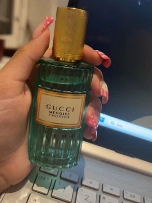 Gucci Mémoire d’Une Odeur parfym - Gucci Mémoire d’Une Odeur parfym i en elegant grön glasflaska med räfflad design och guldfärgad kork. Flaskan har en lyxig vintagekänsla och etiketten är i vitt och guld. Perfekt för dig som gillar exklusiva dofter och snygg design på parfymflaskan.