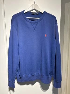 Blå sweatshirt från Polo Ralph Lauren - Klassisk blå sweatshirt från Polo Ralph Lauren med rund halsringning och den ikoniska röda logon broderad på bröstet. Storlek L men passar även M. Skriv vid minsta fundering!!✅