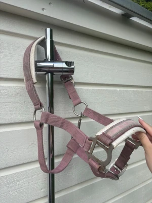 Rosa grimma  - Säljer denna rosa grimma i tyg för häst. Grimman har silvriga metalldetaljer och ett mönster med små söta dödskallar på nosremmen. Justerbar passform. Passar till C ponny. Lite defekter tex att det rostat lite 