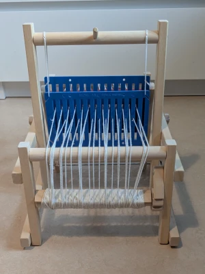 Vävstol i trä med garn för barn , MICKI - En vävstol i ljust trä med blå plastdetalj och tre garnspolar i rött, blått och gult. Perfekt för att skapa egna vävda projekt. Kompakt och enkel att använda, passar både nybörjare och den som vill testa på vävning. På sista bilden syns det att min dotter har ritat lite grann på två ställen med en penna. Man kanske måste zooma in på sista bilden för att se det hon har ritat.