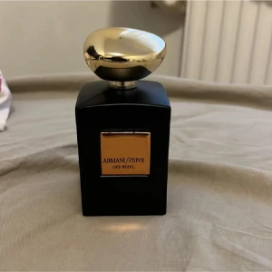 Armani/Privé Oud Royal parfym - Lyxig parfymflaska i svart glas med guldfärgat lock och guldfärgad etikett på framsidan. Flaskan har en elegant, fyrkantig form och utstrålar exklusivitet. Doften är Oud Royal, vilket ger en orientalisk och djup karaktär.