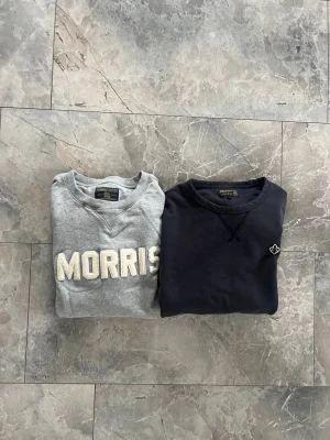 Två Morris sweatshirts  - Säljer två snygga sweatshirts från Morris. En är grå med stor MORRIS-text i vitt på bröstet och den andra är marinblå med en liten broderad logga. Båda har rund hals och klassisk sweatshirt-look. Perfekta till jeans eller chinos.