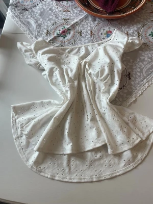 Vit blus med broderade detaljer och knyt🤍 - Söt vit blus med v-ringning, broderade hål och knyt framtill. Blusen har korta volangärmar och är tillverkad i ett lätt bomullstyg som passar perfekt till sommaren. Luftig och flowy passform som ger en romantisk vibe.🤍