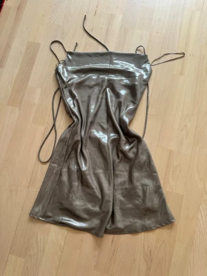Champagnefärgad satin slipklänning - Säljer en glansig champagnefärgad slipklänning i satin med tunna axelband och enkel, rak siluett. Perfekt för dig som gillar minimalistisk och trendig stil. Klänningen har en mjuk, följsam känsla och ger en lyxig look.