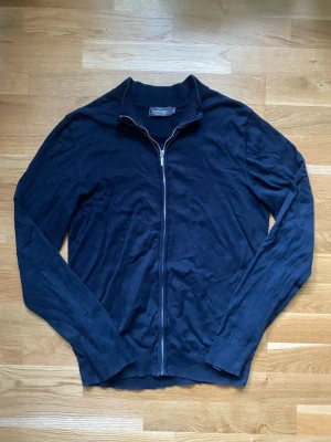 Dressman Full zip - Snygg och clean mörkblå hel-zip som passar perfekt till en enkel/stilren outfit. Okej skick och lätt att matcha med både jeans och andra byxor.