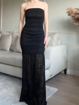 Svart axelbandslös långklänning NA-KD - Snygg svart axelbandslös långklänning med figurnära passform. Klänningen har en tight överdel och en lång, transparent spetskjol som ger en elegant look. Perfekt för dig som vill sticka ut med en stilren och trendig outfit. Helt ny & oanvänd köpt för 599kr 
