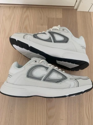 Vita Dior B30 - Snygga vita Dior B30 med chunky sula och grå detaljer på sidorna. Skorna har en sportig vibe med mesh och syntetmaterial, samt svart yttersula för extra kontrast. Perfekta för dig som gillar en clean och modern look.