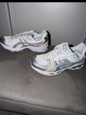 asics gel kayano 14 white blue - Snygga sneakers från Asics i vitt med silvriga och grå detaljer. Skorna har en sportig design med mesh och syntetmaterial, samt klassisk Asics-logga på sidan. Perfekta för en trendig och bekväm stil.