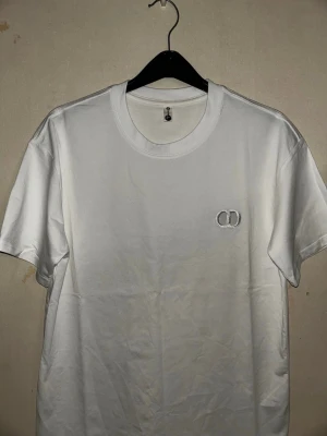  CD t-shirt - Snygg vit t-shirt i bomull med rund hals och diskret broderad logga på bröstet. Enkel och stilren design som passar till det mesta. Perfekt basplagg för garderoben.