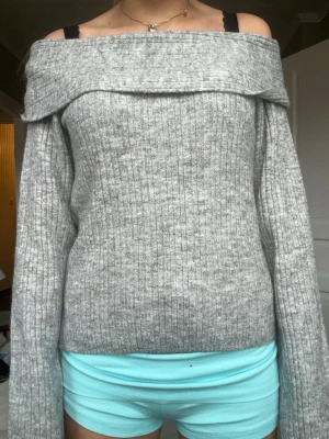 Grå off shoulder stickad tröja - Säljer en ribbstickad grå off shoulder-tröja med bred krage. Tröjan har långa ärmar och en mjuk, mysig känsla. Perfekt för dig som gillar en avslappnad men ändå trendig stil.