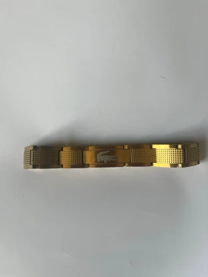 Lacoste armvand-guld - Säljer mitt Lacoste armband i rostfritt stål. Jag har bara använt det ett fåtal gånger därav det mycket bra skicket. Det är 20 cm långt och går att förkorta till 18 cm med länkarna som syns på bilderna. Hör av er om mer frågor! Mvh Loke 