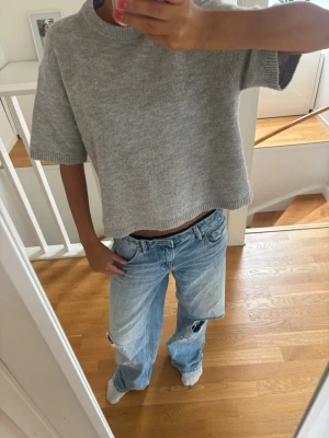 Grå kortärmad stickad tröja - Säljer en grå, kortärmad stickad tröja med boxy passform och ribbade detaljer vid hals, ärmslut och nederkant. Tröjan har en avslappnad look och är perfekt att styla med jeans eller kjol. Materialet är mjukt och bekvämt. Nyskick.