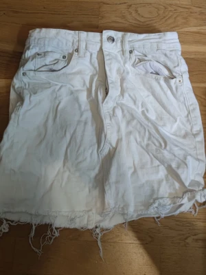 Vit Gina Tricot "Perfect Jeans" kjol strl 38 - Säljer en jättefin vit jeanskjol från Gina Tricot (Perfect Jeans-serien) i storlek 38. Klassisk modell med stretch som sitter superbra, samt en snyggt fransad rå nederkant. Perfekt basplagg till sommaren!