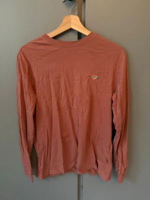 Rostbrun långärmad topp från Dickies - Säljer en rostbrun långärmad topp från Dickies med rund halsringning och liten logga på bröstet. Tillverkad i mjuk bomull, perfekt för en chill och avslappnad stil.