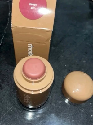 Rhode blush stick Sleepy Girl - Krämrouge i stickformat från Rhode i nyansen Sleepy Girl. Färgen är en mjuk, rosabrun ton som ger ett naturligt fräscht glow till kinderna. Praktisk rund förpackning i beige plast med skruvlock, enkel att ta med i väskan.