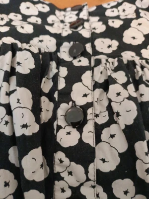 Svart/vit blommig kjol - Superfin blommig knälång kjol i storlek S. Endast använd ett fåtal gånger men kan behöva strykas lite, och endast små skrapor på några av knapparna. Skriv on du har någon fråga🤗