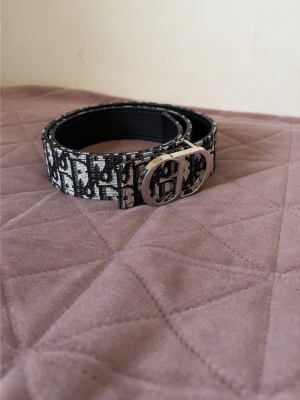Bälte - Snyggt svart och vitt bälte med grafiskt mönster och en stor, rundad silverfärgad spänne framtill. Bältet har en bred design och är gjort i skinn med textil på ovansidan. Perfekt för att lyfta vilken outfit som helst.