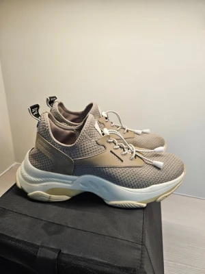 Steve Madden Sneakers Taupe - Ett par sneakers från Steve Madden i färgen taupe. Skorna har en ovandel i textil och TPU, samt en yttersula i syntet. De är designade med snörning och en robust sula.  Storlek 41 men är små i storleken, jag har vanligen 39/40.  Säljes då dem inte använts på länge och inte kan användas då jag har ryggproblem och behöver mer ergonomiska skor.