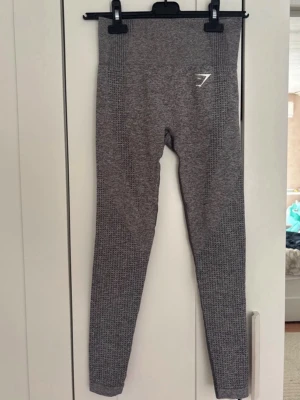 Grå sömlösa tights från Gymshark - Snygga grå sömlösa tights från Gymshark med hög midja och diskret mönster längs benen. Tillverkade i stretchigt funktionsmaterial som andas, perfekta för träning eller gym. Gymshark-logga i vitt på höften och vristen.  I fint skick, men köpa secondhand så vet ej hur mycket de använts(dock inga synligare tecken på användning)