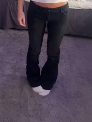 Svarta bootcut jeans - Säljer ett par svarta bootcut jeans med låg midja och klassisk femficksdesign. Jeansen har en snygg utsvängd passform nedtill och är perfekta till crop tops eller hoodies. Materialet känns mjukt och stretchigt för extra komfort.
