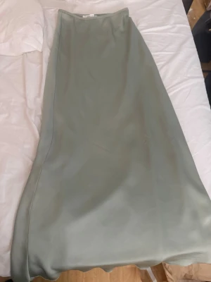 Ljusgrön långkjol i satin - Supersnygg ljusgrön långkjol i satin med slät och glansig yta. Kjolen har en enkel och stilren design som ger en elegant look. Perfekt att styla med en crop top eller stickad tröja för en trendig vibe.