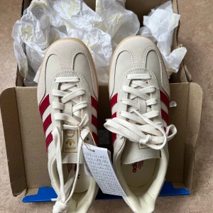 Adidas gazelle indoor med röda ränder - Snygga Adidas sneakers i beige mocka med klassiska röda ränder på sidorna och gummisula. Skorna har lågt skaft och vita snören. Helt nya och aldrig använt, endast testade inomhus. 